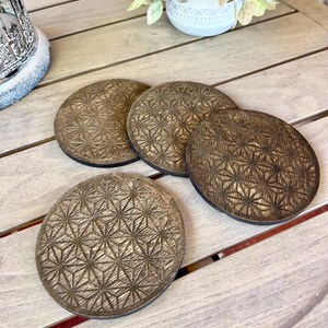 May include: Four round, wooden coasters with a geometric pattern. The coasters are a warm brown color with a dark brown border. The coasters are arranged on a light-colored wooden surface.