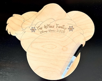 Könnte beinhalten: Ein hölzernes Disney World-Souvenir in Form von Mickey Mouses Kopf und Ohren, mit dem eingravierten Text "The Wible Family Disney World 2025". Ein schwarzer Sharpie-Marker liegt auf dem hellen Holz. Familien-Souvenir.