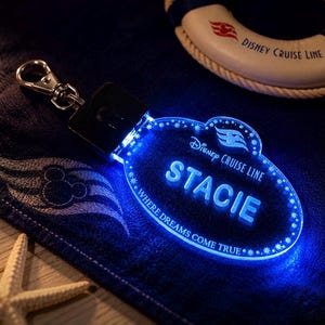 May include: A clear acrylic keychain with a silver metal lobster clasp, illuminated by a bright blue LED light. The keychain features the text Disney Cruise Line, the name STACIE, and the phrase WHERE DREAMS COME TRUE, accented by star motifs.