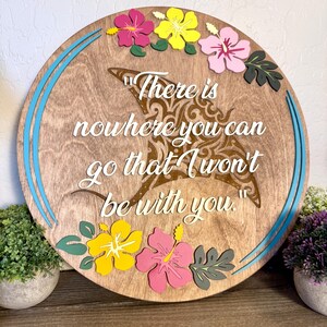 May include: Round wooden sign with a light brown finish, featuring a decorative manta ray design and the quote "There is nowhere you can go that I won't be with you." The sign is adorned with colorful hibiscus flowers and blue accents.