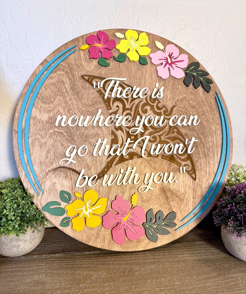 May include: Round wooden sign with a light brown finish, featuring a decorative manta ray design and the quote "There is nowhere you can go that I won't be with you." The sign is adorned with colorful hibiscus flowers and blue accents.