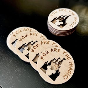 May include: A set of five wooden round ornaments with a Mickey Mouse silhouette and the words "You are the magic" engraved on each. The ornaments are stacked on top of each other.
