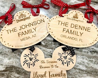 May include: Three wooden name tags with red and white polka dot ribbon. The first tag says "Disneyland" and "The Johnson Family, Mesa, AZ, Where Dreams Come True". The second tag says "Walt Disney World" and "The Denne Family, Orlando, FL, Where Dreams Come True". The third tag is shaped like Mickey Mouse ears and says "This Stroller Belongs To The Lloyd Family".
