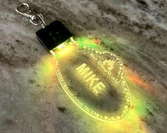May include: A clear plastic light-up name tag with the text "Walt Disney World" and "Where dreams come true" around the edge. The name "Mike" is in the center of the tag. The tag is lit up with a yellow and green glow.