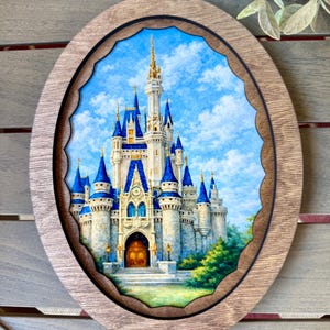 May include: An oval wooden framed artwork featuring a detailed painting of a fairytale castle with blue turrets and a golden spire against a blue sky. The frame has a scalloped inner edge.