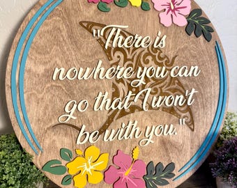 May include: A circular wooden wall sign featuring a cutout manta ray silhouette with intricate patterns. The text reads, "There is nowhere you can go that I won't be with you." The sign is decorated with colorful hibiscus flowers in pink and yellow.
