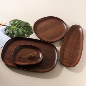May include: A collection of wooden serving platters in various shapes and sizes. The platters are a rich, dark brown color, showcasing the natural wood grain. The set includes oval, round, and rectangular designs, perfect for serving food or displaying decorative items.
