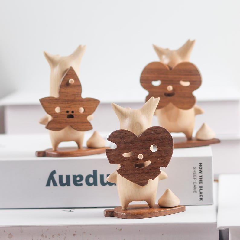 May include: Three wooden figurines with different facial expressions and unique wooden masks. The masks are a heart, a leaf, and a flower. The figurines are standing on wooden bases.
