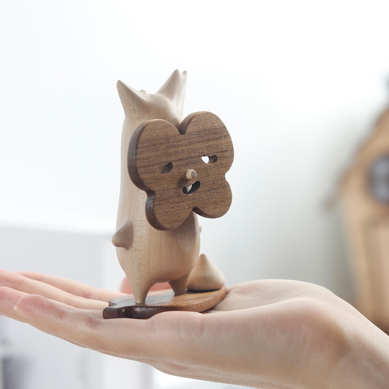 May include: A wooden figurine of a cartoon animal holding a heart-shaped wooden cutout with a smiling face. The figurine is standing on a small wooden base.