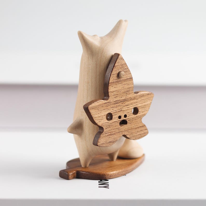 May include: A wooden figurine of a cartoon animal with a leaf-shaped back. The leaf is brown and has a face carved into it. The figurine is standing on a leaf-shaped base.