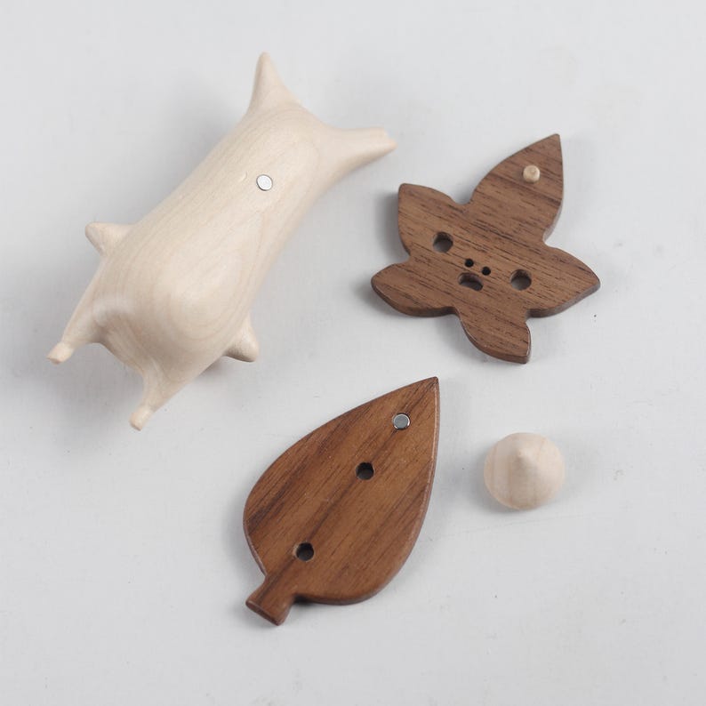 May include: Four wooden ornaments, two are leaf shaped and two are animal shaped. The leaf shaped ornaments are made of dark wood and the animal shaped ornaments are made of light wood.