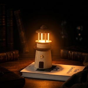 May include: A wooden lighthouse-shaped lamp with a warm, inviting glow. The lamp features a light brown body, a dark brown top, and a small door. It sits on a book with the words "Time Limitless" visible. The lamp is approximately 6 inches tall.