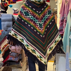May include: A black hooded poncho with a colorful geometric pattern and fringe. The poncho is made of wool and has a traditional design.