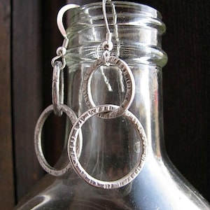 May include: Silver earrings with two circular designs. The earrings are hanging from a glass bottle.