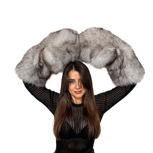 May include: A pair of luxurious, silver-gray fur arm warmers. The fur appears soft and fluffy, with varying shades of gray. The arm warmers are held up against a white background.