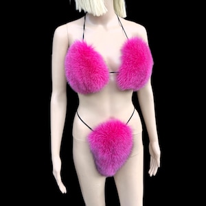 Puede incluir: Un conjunto de bikini de piel rosa intenso. El top del bikini tiene copas triangulares y la parte inferior es de estilo tanga. El conjunto se exhibe en un maniquí sobre un fondo negro.