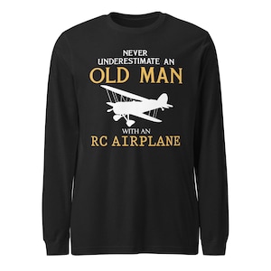 May include: Black long-sleeve t-shirt with the text "Never underestimate an old man with an RC airplane" in white and yellow. A white silhouette of a small airplane is in the center of the shirt.
