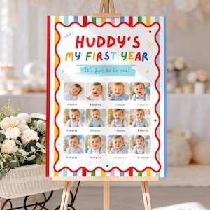 Puede incluir: Un póster de hitos en un caballete de madera con el texto HUDDY'S MY FIRST YEAR y It's fun to be one! El diseño incluye un borde rojo ondulado, rayas verticales coloridas y doce espacios para fotos etiquetados de 1 a 12 meses.