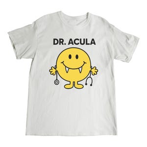 May include: White t-shirt with a yellow smiley face with fangs and a stethoscope. The text "DR. ACULA" is printed above the smiley face.