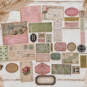 May include: A collection of vintage-style paper ephemera including labels, tickets, playing cards, and receipts in shades of pink, green, and beige. The items feature various printed text, floral illustrations, and numerical designs for scrapbooking.