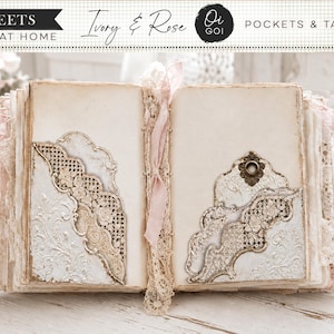 May include: An open journal featuring ivory pages with decorative lace-trimmed pockets and tags. The spine is bound with a light pink ribbon. The pages display intricate embossed floral patterns and ornate die-cut edges in cream and white tones.