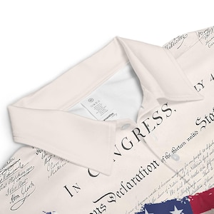 May include: A white polo shirt featuring a print of the Declaration of Independence and a small American flag. The text "IN CONGRESS, ..." is visible on the shirt.