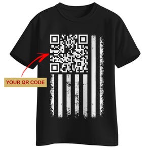 Op de afbeelding: Zwart T-shirt met een verweerd Amerikaans vlagontwerp en een QR-code in de linkerbovenhoek. De tekst "YOUR QR CODE" staat in een gouden rechthoek. Het vlagontwerp heeft witte strepen en een witte QR-code.