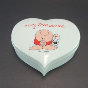 May include: A light blue heart-shaped trinket box with a cartoon illustration of a man and a dog. The box has the text "my treasures" and "Tom Wilson" on it.