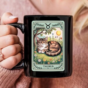 May include: Black ceramic mug with a white design featuring a cat with a Taurus zodiac symbol and the text "Taurus".