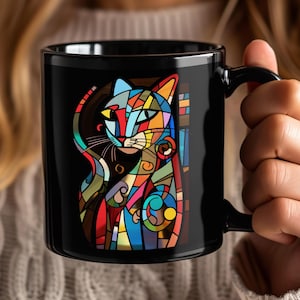 May include: Black ceramic mug with a colorful abstract cat design. The cat is made up of geometric shapes in shades of red, blue, yellow, green, and black.