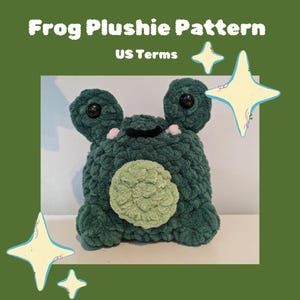 May include: A green crocheted frog plushie with black eyes and a light green belly. The plushie is sitting on a white surface. The text "Frog Plushie Pattern US Terms" is at the top of the image.