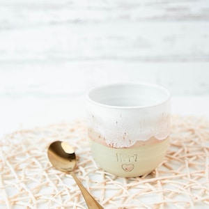 Könnte beinhalten: Eine weiße Keramiktasse mit hellgrünem und rosafarbenem Überzug. Die Tasse hat das Wort "Herz" mit einem Herzsymbol darauf geschrieben. Die Tasse steht auf einem geflochtenen Untersetzer mit einem goldenen Löffel daneben.