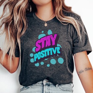 Camiseta "Stay Positive", camiseta gráfica motivacional, camiseta retrô com letras em formato de bolha, presente com citação inspiradora, camiseta inspiradora e colorida