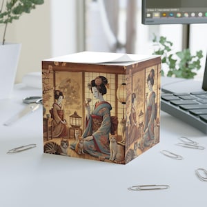 May include: A square notepad with a Japanese geisha design. The image shows geishas in traditional dress, accompanied by cats, tea sets, and lanterns. The colour scheme features soft browns, blues, and reds, creating a calm and cultural aesthetic.