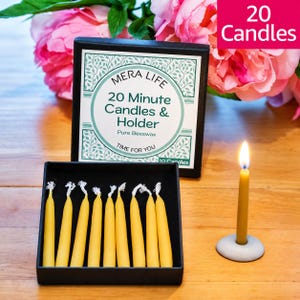 May include: A black box containing yellow beeswax candles with a label reading MERA LIFE 20 Minute Candles & Holder Pure Beeswax TIME FOR YOU. A single lit yellow candle stands in a small gray circular holder next to the box.