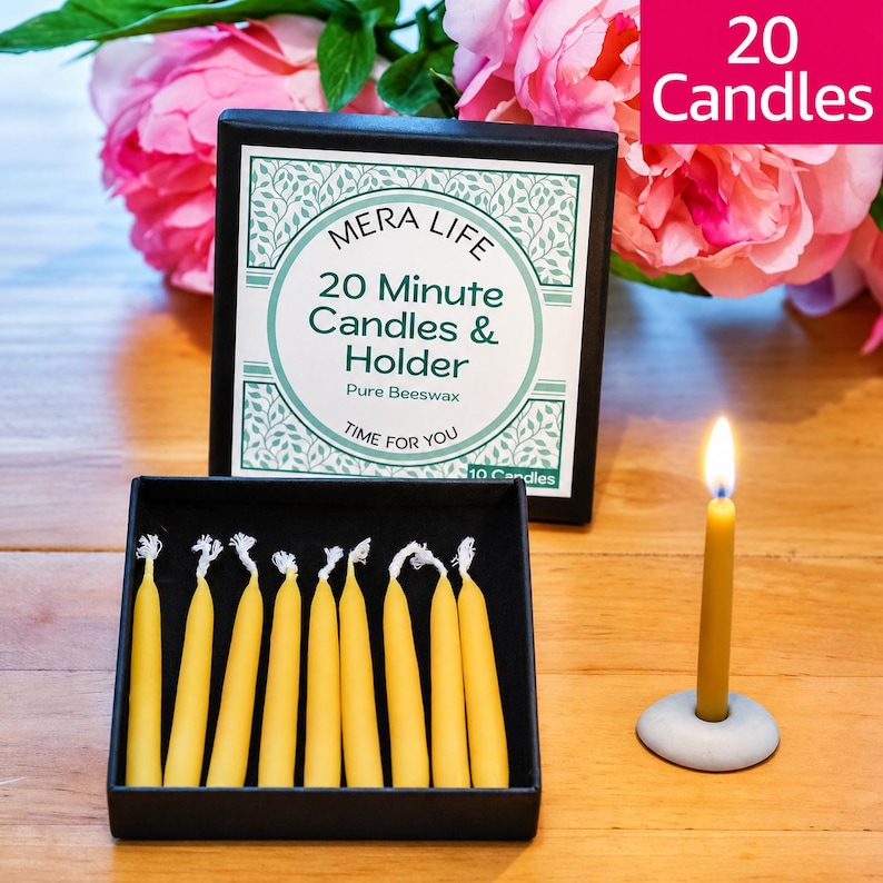 May include: A black box containing yellow beeswax candles with a label reading MERA LIFE 20 Minute Candles & Holder Pure Beeswax TIME FOR YOU. A single lit yellow candle stands in a small gray circular holder next to the box.