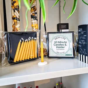 May include: A set of ten yellow beeswax candles in a black box, with one candle standing in a white circular holder. The packaging features the text MERA LIFE 20 Minute Candles & Holder Pure Beeswax TIME FOR YOU 10 Candles on a white label.