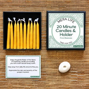 May include: A set of ten yellow beeswax candles in a black box with a lid labelled MERA LIFE 20 Minute Candles & Holder Pure Beeswax. Includes a white card with printed text and a small white oval candle holder for a single taper candle.