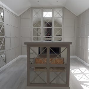 May include: A white room with a large mirrored wardrobe with a geometric pattern. The wardrobe is in the centre of the room and there is a wooden divider in front of it.