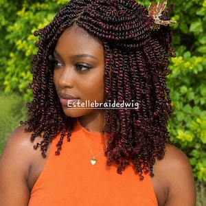 May include: A shoulder-length braided wig featuring dark black and deep burgundy red twisted strands. The hair is styled with a gold-toned butterfly hair clip on the side. The text Estellebraidedwig is visible across the centre of the image.