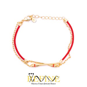 May include: A red and gold bracelet with a delicate chain and a red cord. The bracelet features a gold bar with red accents.