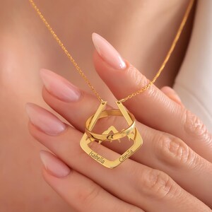 May include: Gold necklace featuring a mountain design and two rings. The rings are engraved with the names "Isabella" and "Camila".