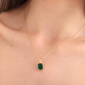 May include: A gold chain necklace with a green emerald-shaped pendant.
