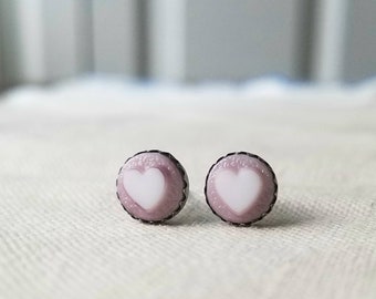 May include: A pair of small, silver stud earrings with a pink and white heart design.