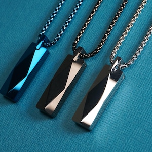May include: Three geometric pendant necklaces. The pendants are rectangular with a faceted design, in black, silver, and blue. Each pendant hangs from a matching chain. The background is a solid teal color.