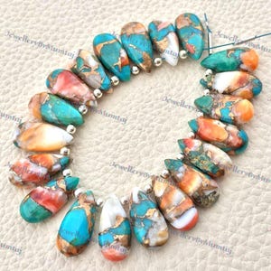 May include: Strand of teardrop-shaped beads in shades of turquoise, orange, white, and brown, with gold-colored accents. The beads are strung together with small silver-colored beads. The image has the text "JewelleryByMumtaj".