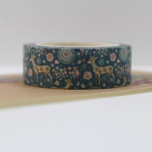 May include: A roll of decorative washi tape featuring a teal background with a repeating pattern of deer, flowers, and other botanical elements. The tape is on a light brown surface.