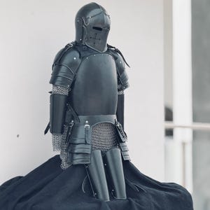 May include: A black knight's armor set, including a helmet, breastplate, chainmail, and leg guards. The armor is made of metal and has a dark, weathered finish.