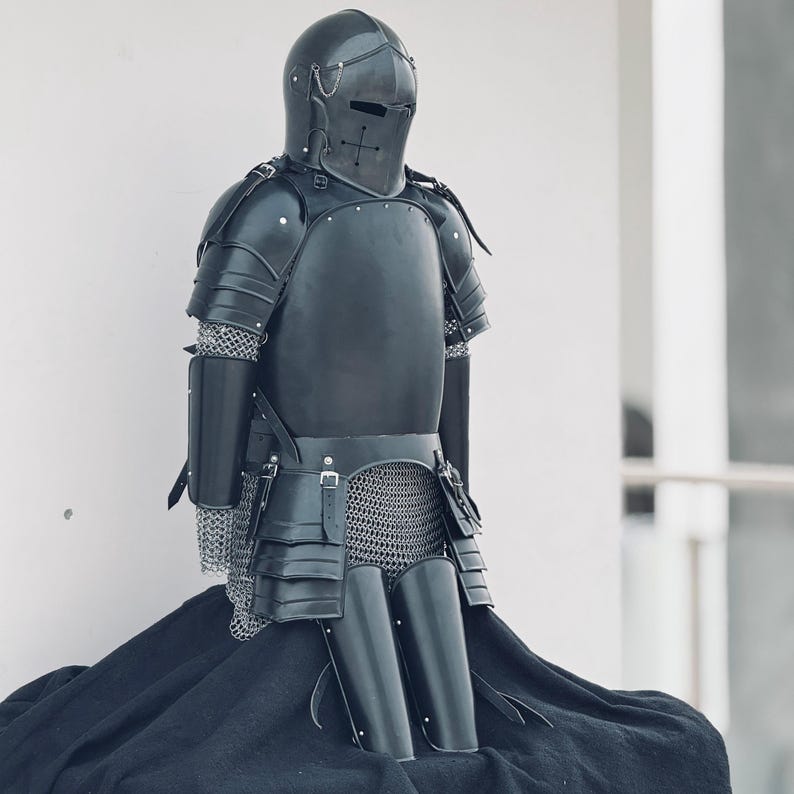 May include: A black knight's armor set, including a helmet, breastplate, chainmail, and leg guards. The armor is made of metal and has a dark, weathered finish.