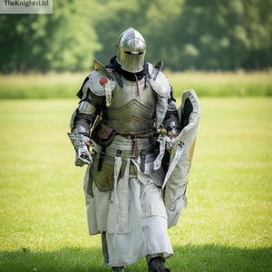 May include: A person in full medieval armor, including a helmet, chest plate, and leg guards, stands on a grassy field. The armor is silver and detailed, with a shield and a sword. The KnightsLtd logo is in the top left corner.
